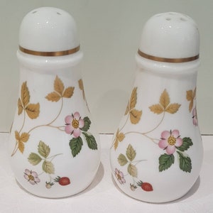 Può includere: Un paio di saliere e pepiere in ceramica bianca. Ogni shaker presenta una fascia dorata e un motivo a vite di fragole. Il design include fiori rosa, foglie verdi e fragole rosse mature. Un classico accessorio da cucina.