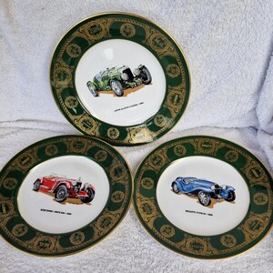 Puede incluir: Tres platos decorativos con bordes dorados y fondos verdes. Cada plato presenta un coche antiguo en el centro. El plato superior presenta un coche verde con el texto "ALFA ROMEO 8C 2300 - 1932". El plato del medio presenta un coche rojo con el texto "BENTLEY 4 1/2 LITRE - 1929". El plato inferior presenta un coche azul con el texto "BUGATTI TYPE 55 - 1931".