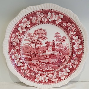 Może przedstawiać: Ozdobny ceramiczny talerz z czerwono-białym wzorem kwiatowym i krajobrazowym. Talerz ma falisty brzeg i szczegółową ilustrację mostu, drzew i budynku. Krawędź talerza jest ozdobiona kwiatami.