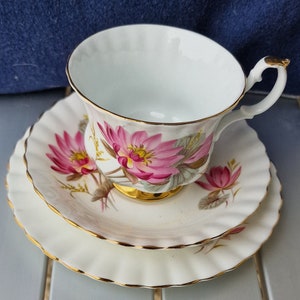 May include: A white teacup and saucer set with a pink floral pattern. The cup and saucer have a gold trim.