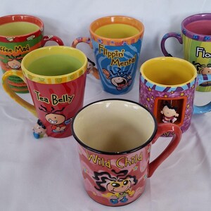 Puede incluir: Seis tazas de cerámica coloridas con personajes de dibujos animados y frases como "Coffee Mad" y "Tea Belly". Cada taza tiene un diseño único, con colores vibrantes e ilustraciones divertidas. Las tazas tienen asas y son aptas para bebidas calientes.