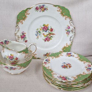 Puede incluir: Juego de té de porcelana vintage con una fuente cuadrada, varios platos redondos, una jarra de crema y un cuenco. Base blanca, borde verde, ribete dorado y diseños florales y de aves.