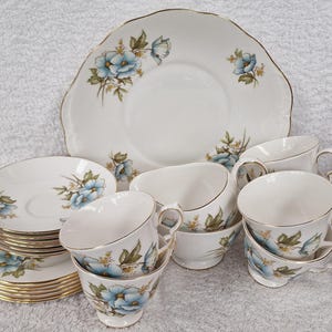 May include: A set of vintage teacups and saucers with a floral design. The cups and saucers are white with a blue and green floral pattern. The set includes a cake plate with the same floral design.