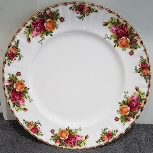 以下が含まれることがあります： 白いセラミックプレート、スカラップエッジとゴールドトリム付き。 プレートは、緑の葉を持つ赤、オレンジ、ピンクのバラのクラスターで飾られています。 食事を提供するクラシックなデザインです。