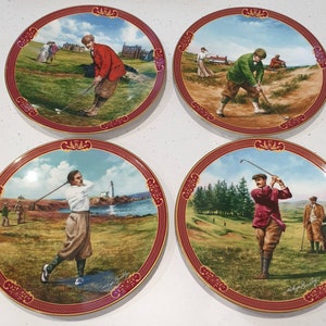 Può includere: Set di quattro piatti in ceramica decorativi che raffigurano golfisti in varie pose su un campo da golf. Ogni piatto ha un bordo rosso e dorato con uno sfondo bianco. I piatti fanno parte di una collezione che celebra lo sport del golf.