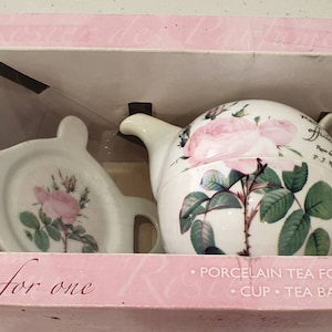 Könnte beinhalten: Porzellan-Teeset für eine Person, bestehend aus Teekanne, Tasse und Teebeutelablage. Das Set ist mit rosa Rosen-Illustrationen und grünen Blättern verziert. Auf der Box steht "Tea for one".