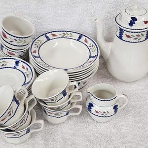 May include: A white ceramic tea set with a floral design. The set includes a teapot, cups, saucers, bowls, and a creamer. The rims of the dishes and the teapot are decorated with blue, red, and green floral patterns.