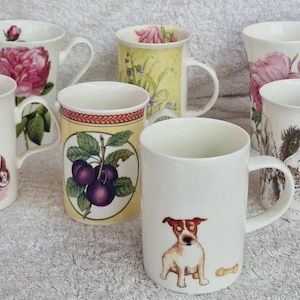 May include: A collection of ceramic mugs with various designs. Some mugs feature floral patterns, while others showcase dog illustrations. The mugs are white with curved handles, suitable for beverages.