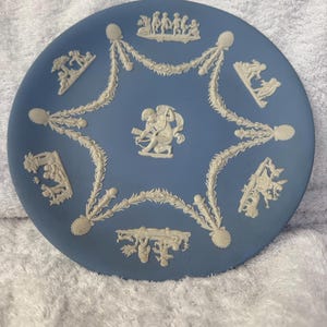 Könnte beinhalten: Ein blauer und weißer Keramikteller mit einem erhabenen Design aus Cherubim und floralen Motiven. Der Teller ist ein klassisches Beispiel für blaues und weißes Transferware.