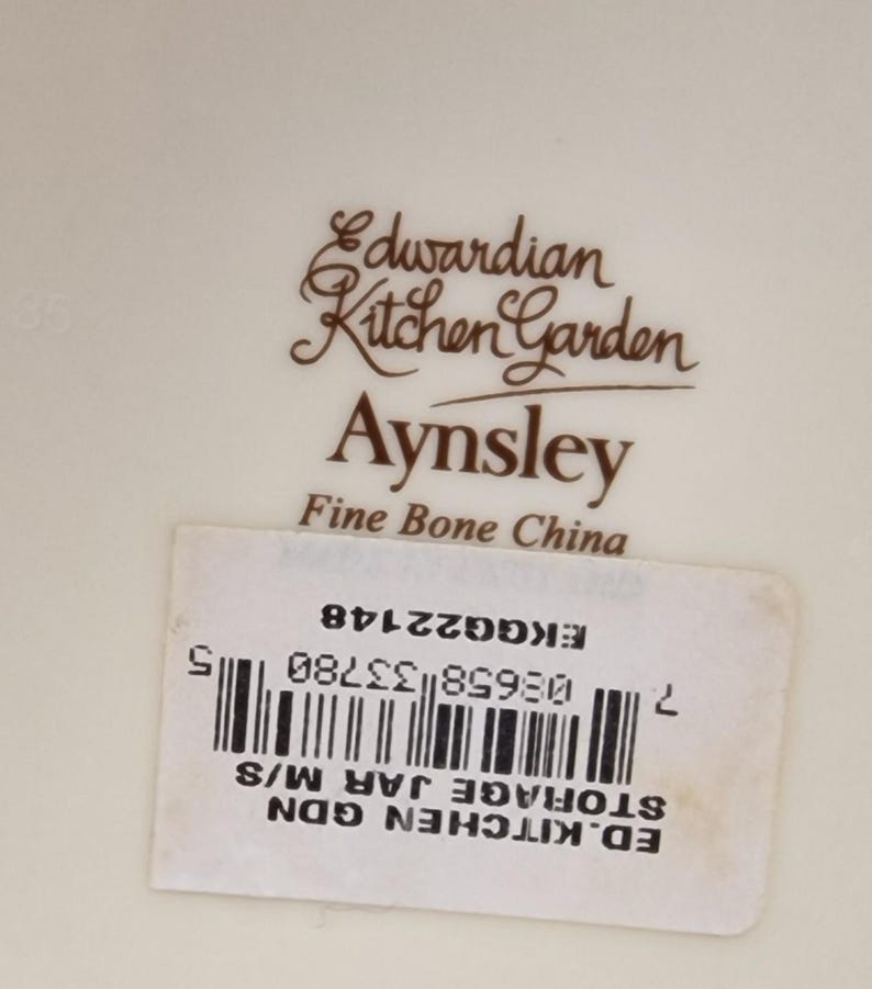 May include: A white ceramic storage jar with a brown Edwardian Kitchen Garden Aynsley Fine Bone China label. The label also includes a barcode and the text "ED. KITCHEN GDN STORAGE JAR M/S 7 08658 33780 5 EKG GG22148".