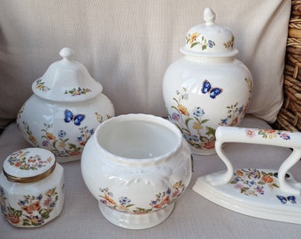 Può includere: Un set di cinque contenitori in ceramica bianca con motivi floreali e farfalle. I contenitori sono di diverse dimensioni e forme, tra cui un barattolo, un barattolo con coperchio, una ciotola e un ferro da stiro decorativo.