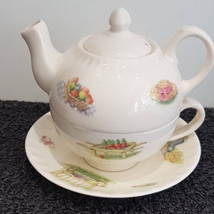 Puede incluir: Un juego de té de porcelana blanca con un diseño floral. La tetera tiene una tapa y un asa. La taza y el platillo tienen un diseño a juego. El juego presenta una cesta de fruta, un sombrero de paja, una carretilla con verduras y una escena de jardín.