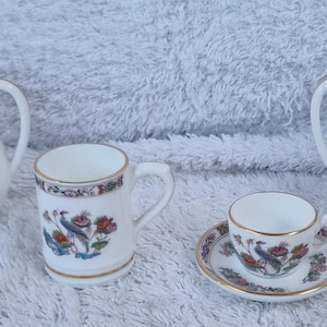 Puede incluir: Juego de té de porcelana blanca con diseño floral y de pájaros. El juego incluye dos teteras, una taza y una taza de té con platillo. Los bordes y los detalles son dorados.