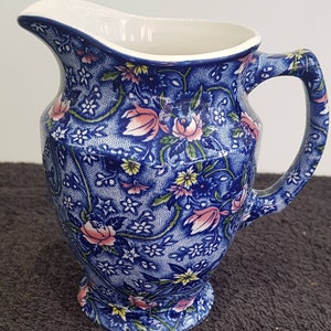 Puede incluir: Una jarra de crema de cerámica azul y blanca con un patrón floral. La jarra tiene un asa y un pico.