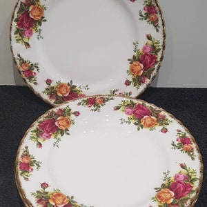 Puede incluir: Un juego de cuatro platos de cena de cerámica blanca con borde dorado y un patrón floral con rosas rojas, rosas y amarillas.