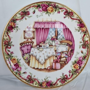 Può includere: Piatto decorativo in porcellana con bordo dorato, raffigurante una scena d'interni dettagliata con un tavolo apparecchiato per il tè, una finestra con tende rosa e un bordo floreale di rose e nastri. Il piatto ha un'estetica vintage.