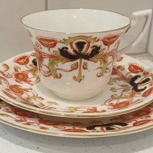 Puede incluir: Un juego de taza y platillo de té blanco con un patrón floral en tonos naranja, verde y negro. El diseño presenta flores y hojas estilizadas.