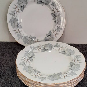 May include: A set of six white ceramic dinner plates with a silver and gold leaf design. The plates have a scalloped edge and a gold rim.