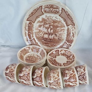 May include: A vintage brown and white dinnerware set featuring a sailing ship design. The set includes plates, bowls, saucers, and cups. The plates have the words "Friendship of Salem" and "U.S. Revenue Cutter" printed on them.