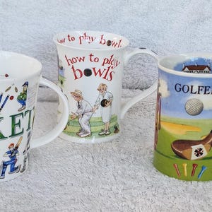 May include: Three white ceramic mugs with sports themes. One mug has the word "CRICKET" with cricket player illustrations. Another says "how to play bowls" with figures playing bowls. The third mug features "GOLFER" with a golf scene.