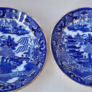 Puede incluir: Dos cuencos de porcelana azul y blanca con borde dorado y un diseño tradicional de paisaje chino.