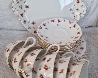 May include: A vintage tea set featuring white porcelain cups, saucers, and a serving plate, all adorned with a delicate pink rose pattern and gold trim. The set includes six cups, saucers, and a large serving plate.