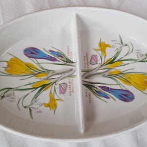 May include: An oval white ceramic divided serving dish featuring botanical illustrations of yellow and purple crocus flowers and white galanthus snowdrop flowers with the printed text Crocus and Galanthus Snow-Drop on both sides of the central divider.