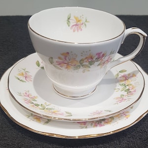 May include: A white teacup and saucer set with a floral pattern of pink and yellow flowers. The set has a gold trim around the edges.