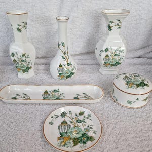 Könnte beinhalten: Ein Set aus sechs weißen Porzellanstücken mit grünen und goldenen Blumendesigns. Das Set enthält zwei Vasen, eine kleine Schale, eine Schmuckdose, ein Tablett und einen kleinen Teller.