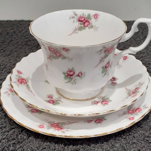 Può includere: Servizio da tè bianco composto da tazza, piattino e piattino da dessert. Il set presenta un motivo floreale di rose rosa e foglie verdi. I bordi sono rifiniti in oro. La tazza ha un manico curvo.