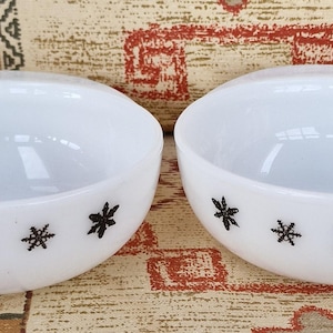 Puede incluir: Dos cuencos de cerámica blanca con diseños de copos de nieve negros. Los cuencos están vacíos y están sobre una superficie estampada.