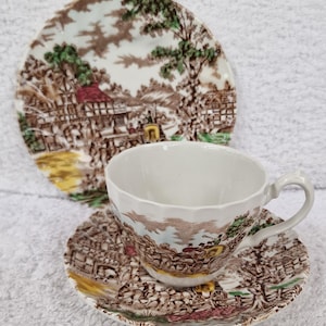 以下が含まれることがあります： 茶色の緑色の花柄のヴィンテージティーカップとソーサーのセット。パターンは、馬車と建物のある田園風景を描いています。