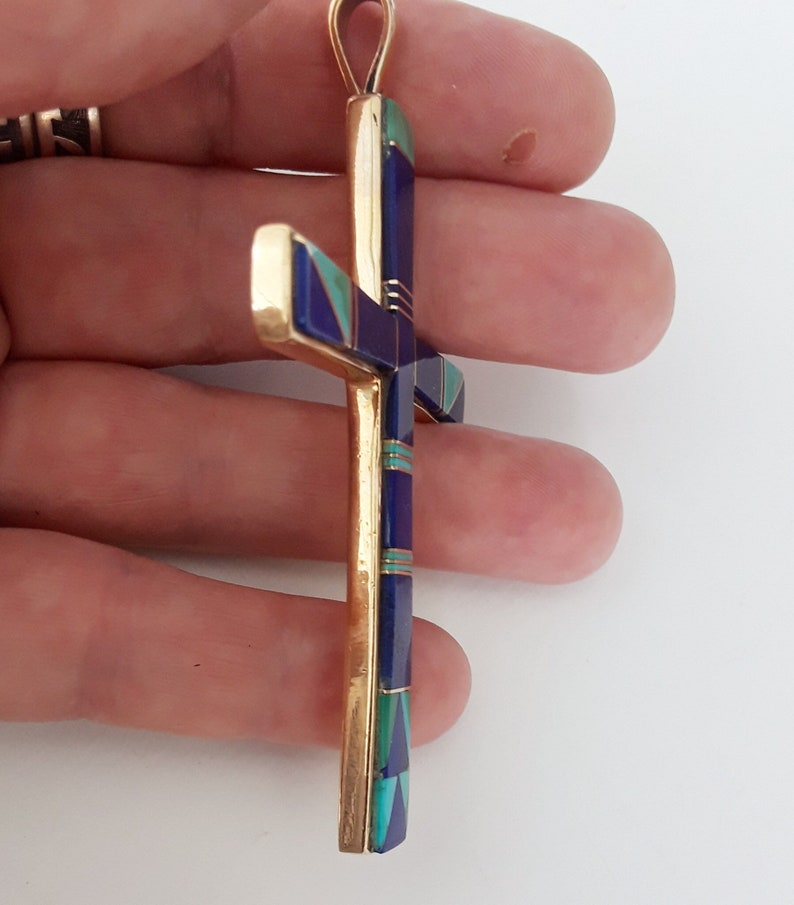 K&ouml;nnte beinhalten: Goldener Anh&auml;nger in Form eines Kreuzes. Das Kreuz hat eingelegte Abschnitte aus blauen, gr&uuml;nen und violetten Steinen. Der Anh&auml;nger hat oben eine Schlaufe f&uuml;r eine Kette.