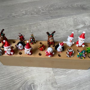 Peut inclure: Un présentoir en bois avec 15 figurines sur le thème de Noël, dont le Père Noël, des pingouins, des rennes et des hommes en pain d'épices. Les figurines sont en pâte polymère et peintes en rouge, blanc, vert et marron.