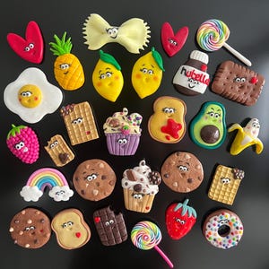 Peut inclure: Une collection d'aimants sur le thème de la nourriture, comprenant un œuf au plat, un ananas, des citrons, un pot de Nutella, un biscuit, un cupcake, une tranche de pain grillé, une fraise et un donut, tous avec des visages.