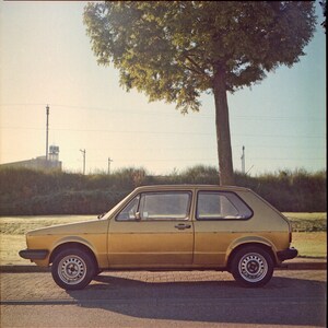 Puede incluir: Un Volkswagen Beetle vintage dorado estacionado en un campo de hierba con un árbol en el fondo.
