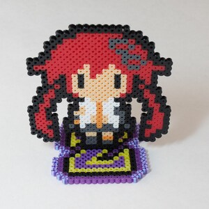 May include: A red-haired anime character with a black and white school uniform, standing on a purple and yellow patterned base. The character is made of perler beads.