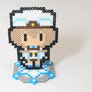 May include: A pixel art figure of a person wearing a white and blue hat with a brown brim and a white shirt with a blue collar. The figure is standing on a blue and gray pixel art base.
