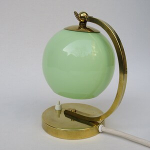 Peut inclure: Une lampe de table en laiton avec un abat-jour en verre vert. La lampe a un bras incurv&eacute; et une base ronde.