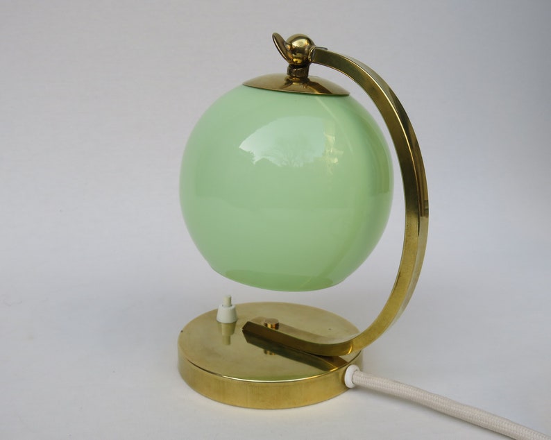 Peut inclure: Une lampe de table en laiton avec un abat-jour en verre vert. La lampe a un bras incurv&eacute; et une base ronde.