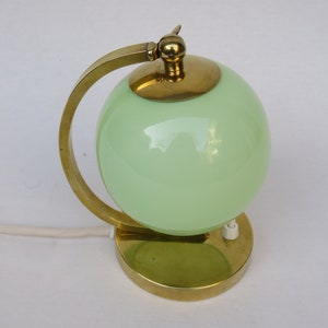 Peut inclure: Une lampe de table en laiton avec un abat-jour en verre vert en forme de globe. La lampe a un bras incurv&eacute; et une base ronde.