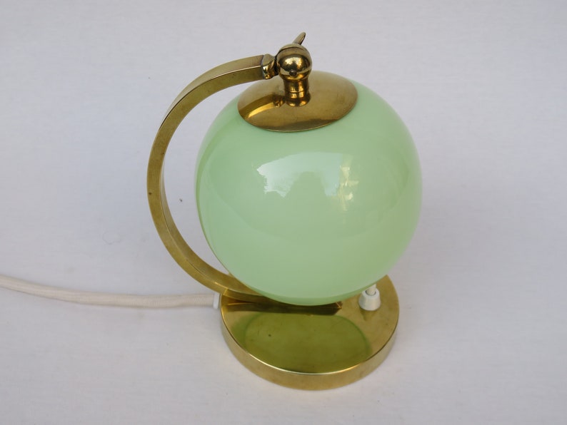 Peut inclure: Une lampe de table en laiton avec un abat-jour en verre vert en forme de globe. La lampe a un bras incurv&eacute; et une base ronde.