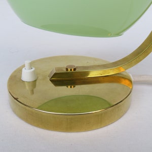 Peut inclure: Une lampe de bureau en laiton avec un abat-jour en verre vert et un interrupteur &agrave; bascule blanc. La lampe a un bras incurv&eacute; et une base ronde.