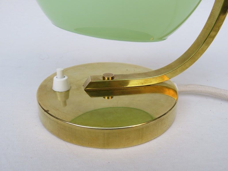 Peut inclure: Une lampe de bureau en laiton avec un abat-jour en verre vert et un interrupteur &agrave; bascule blanc. La lampe a un bras incurv&eacute; et une base ronde.
