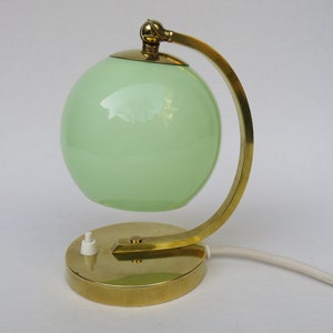 Peut inclure: Une lampe de table en laiton avec un abat-jour en verre vert. La lampe a un bras incurv&eacute; et une base ronde.