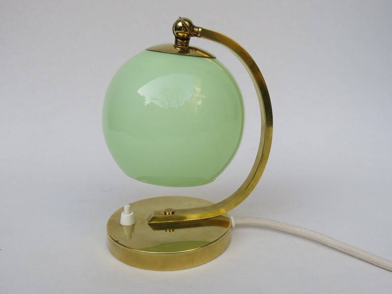 Peut inclure: Une lampe de table en laiton avec un abat-jour en verre vert. La lampe a un bras incurv&eacute; et une base ronde.