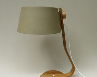 May include: A wooden desk lamp with a curved arm and a beige fabric shade. The lamp has a white cord and a round wooden base.