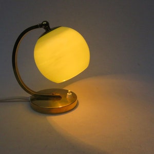 Peut inclure: Une lampe de table en laiton avec un bras incurv&eacute; et un abat-jour en verre jaune.