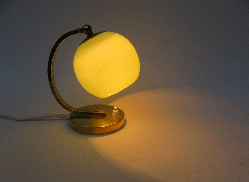 Peut inclure: Une lampe de table en laiton avec un bras incurv&eacute; et un abat-jour en verre jaune.