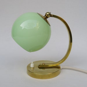 Peut inclure: Une lampe de bureau en laiton avec un abat-jour en verre vert. La lampe a un bras incurv&eacute; et une base ronde.